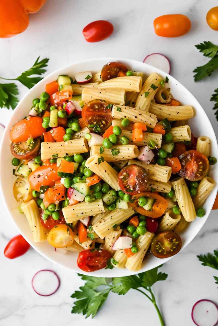 white bowl on a table with veggie pasta salad made with peas and tomatoes