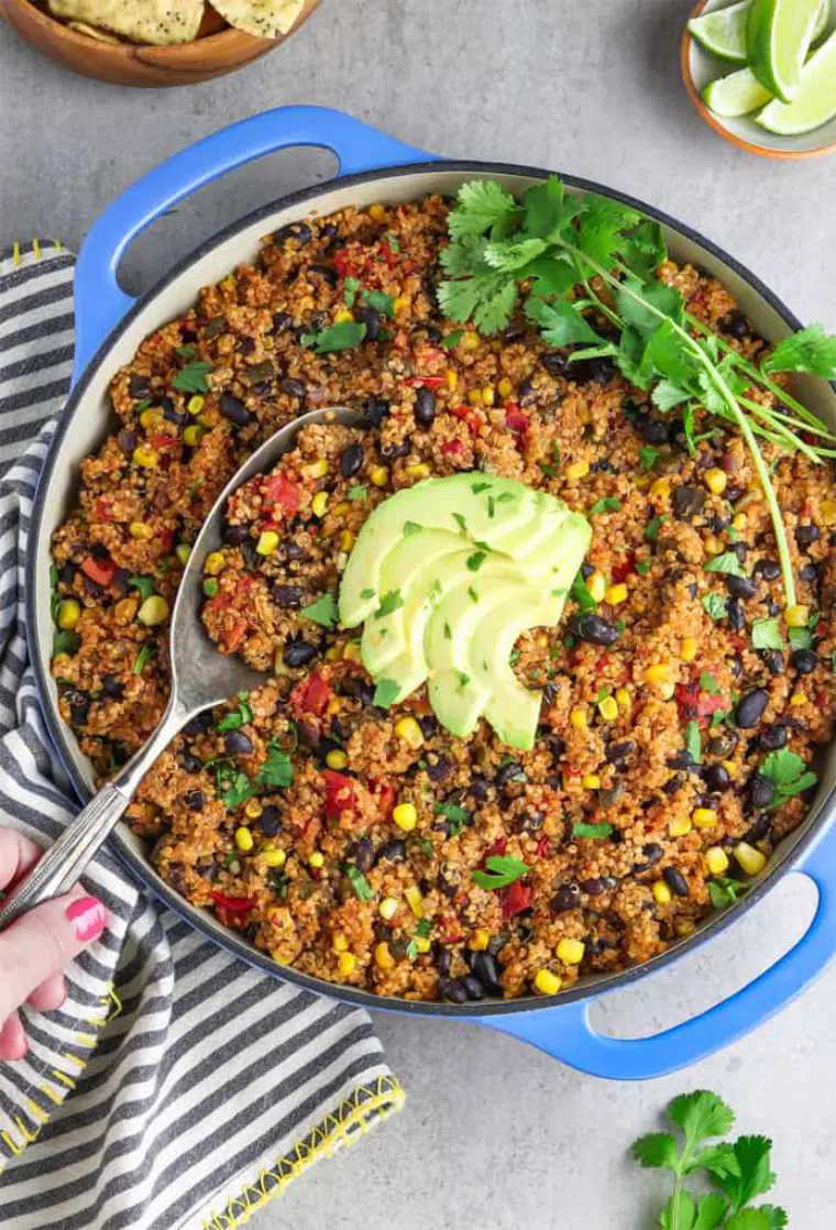 large blue pot with Mexican flavored quinoa, corn, beans, fresh herbs and avocado being scooped