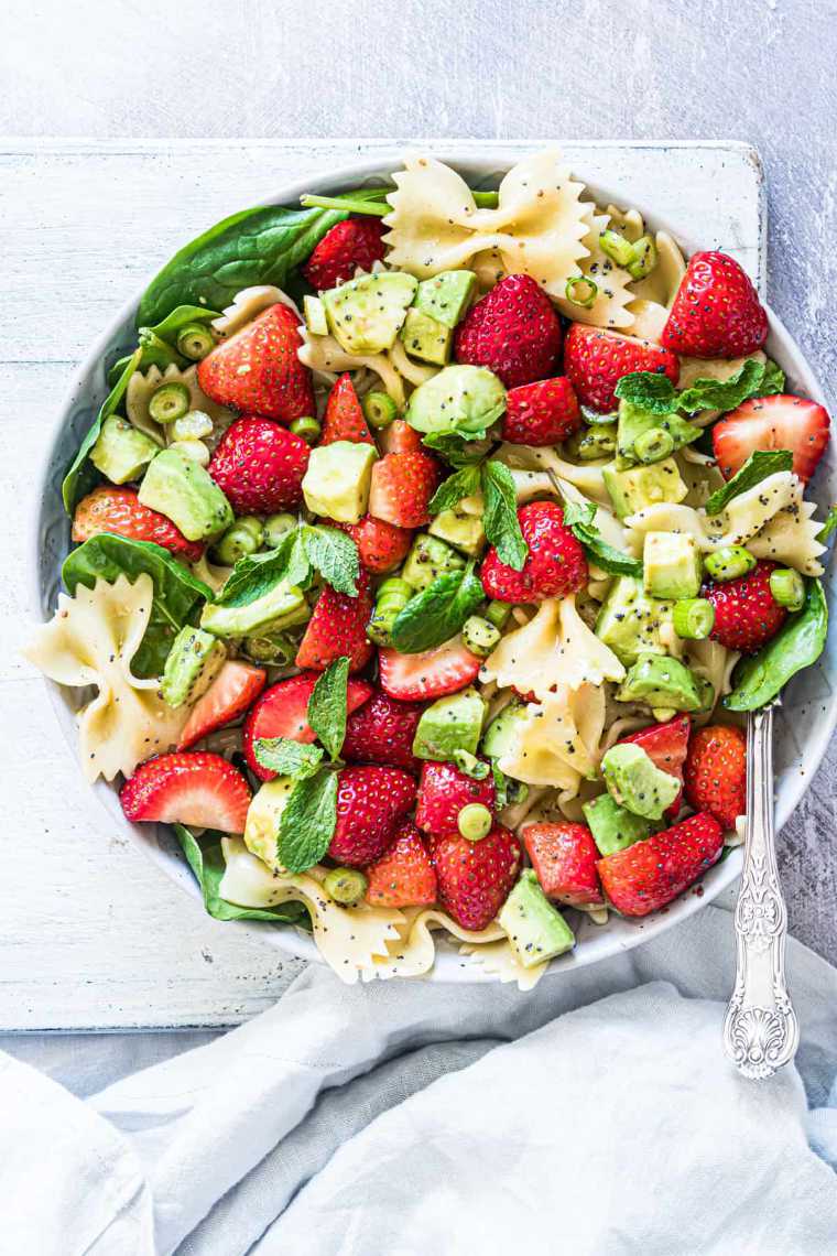 white bowl with a spoon and vegan strawberry avocado pasta salad