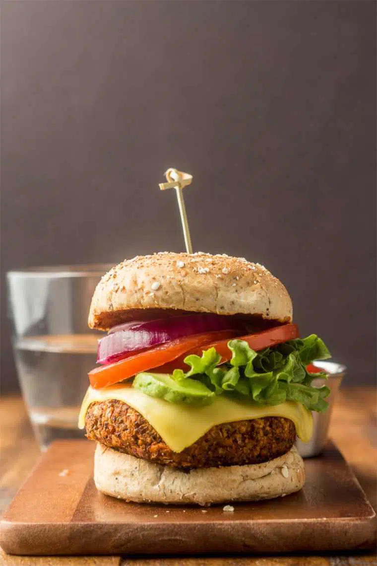 wooden table with a homemade vegan burger featuring a quinoa patty and vegetables