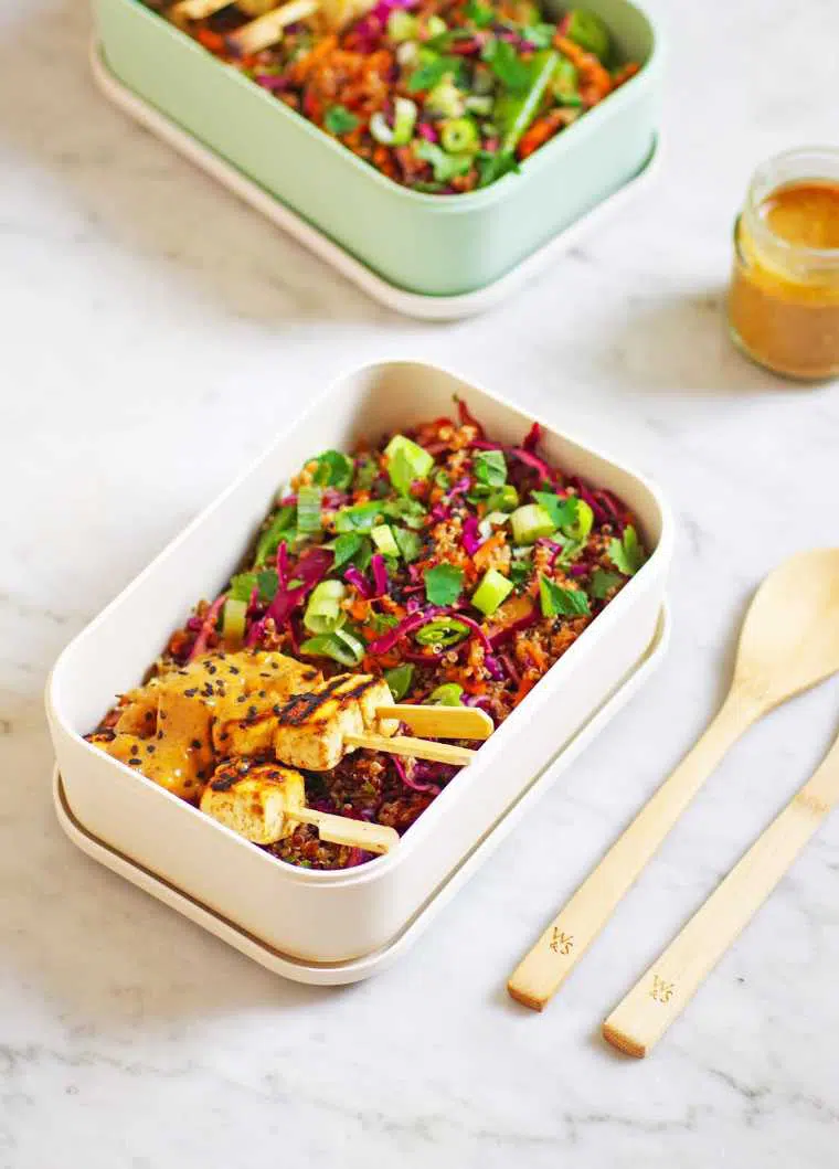 two lunchboxes filled with colorful vegan thai quinoa salad with tofu satay skewers