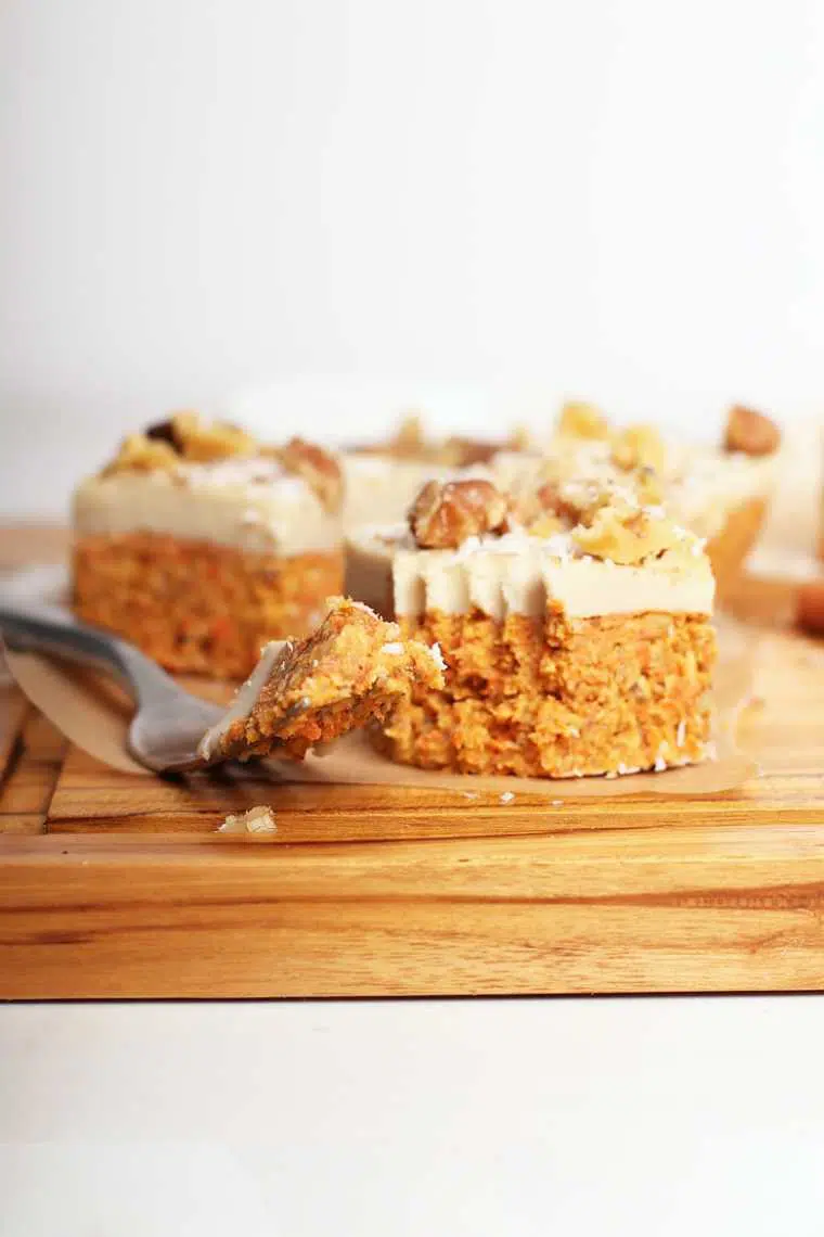 wooden chopping board with several raw vegan carrot cake squares next to a fork