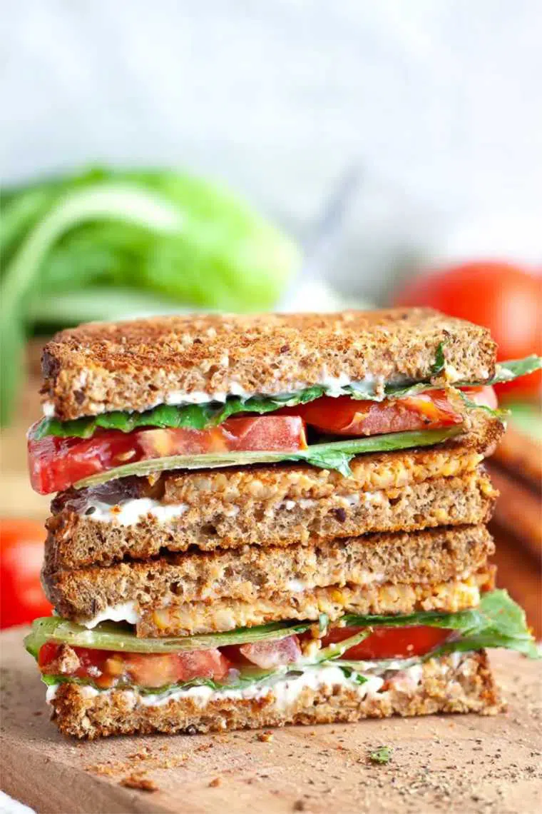 wooden chopping board with two whole grain vegan BLT sandwiches