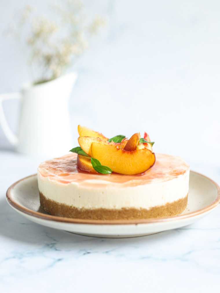 white table with a serving plate featuring vegan no bake peach cheesecake