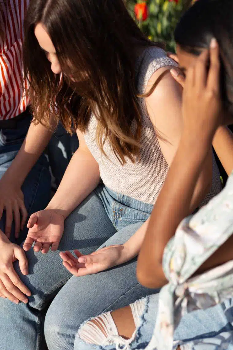 Three women sitting next to each other outside in the sun