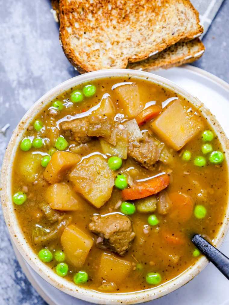 two toasts and a bowl of vegan beef stew with a spoon
