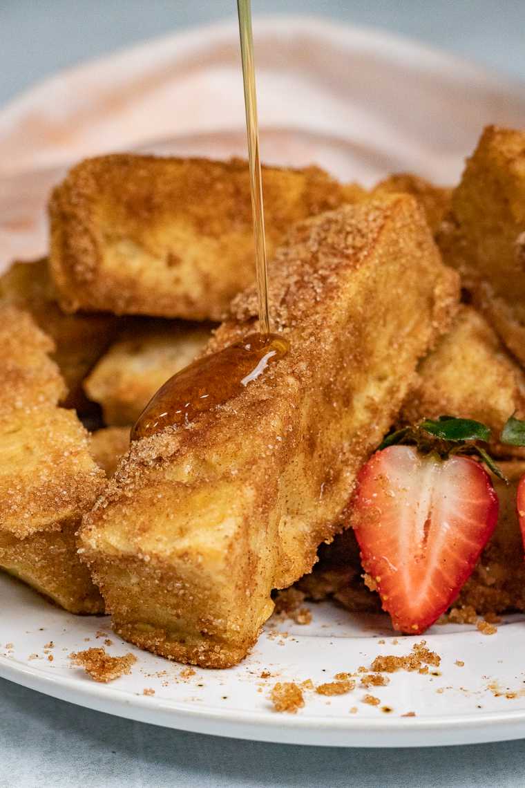 white plate with half a dozen Vegan French Toast Sticks being drizzled with maple syrup
