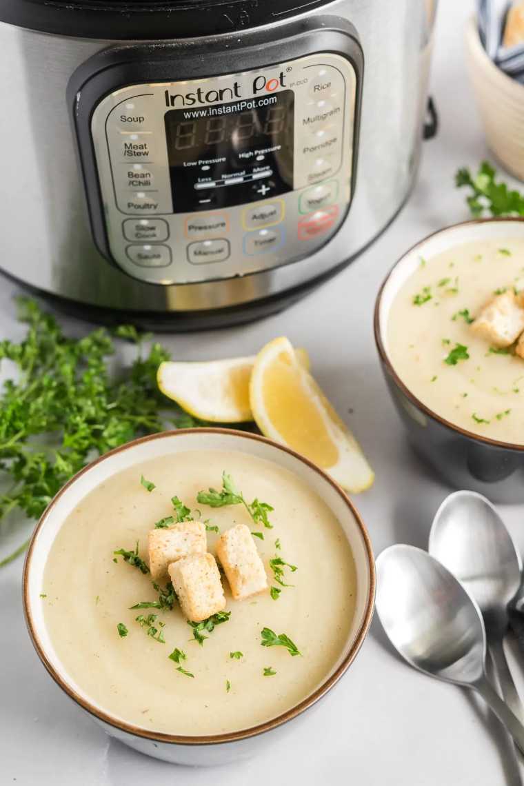 table with an Instant Pot next to two bowls of vegan cauliflower soup