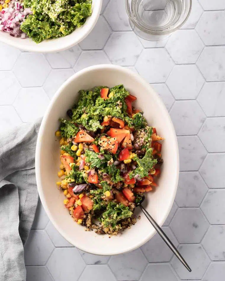 white bowl with kale, corn, onion, quinoa and veggies on a table