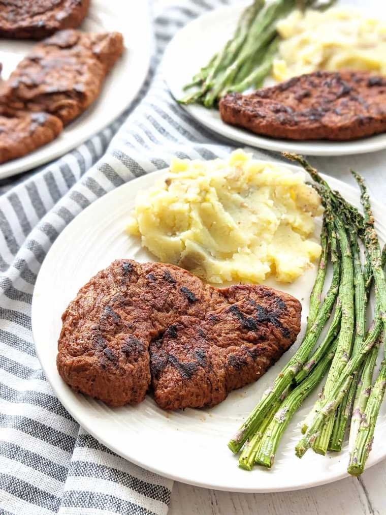 two white plates with grilled asparagus, mashed potatoes and homemade vegan steaks