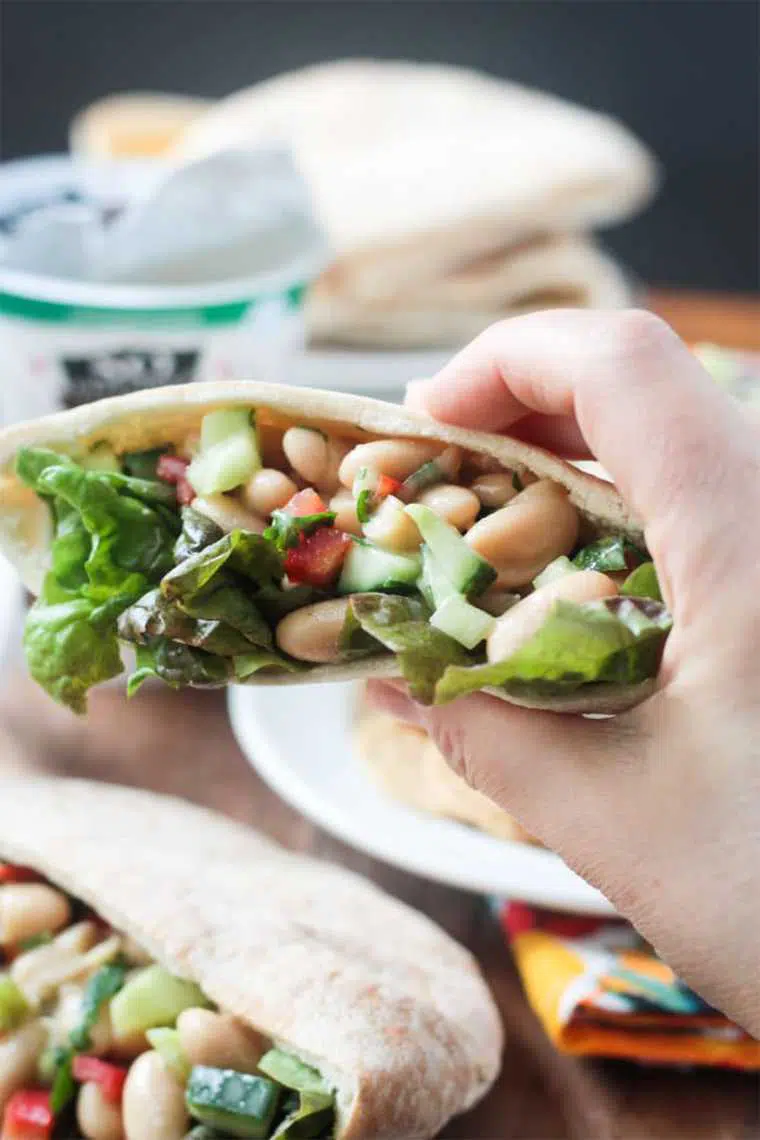 hand holding a pita pocket with salad leaves, cucumber and white beans for an easy vegan cold lunch idea