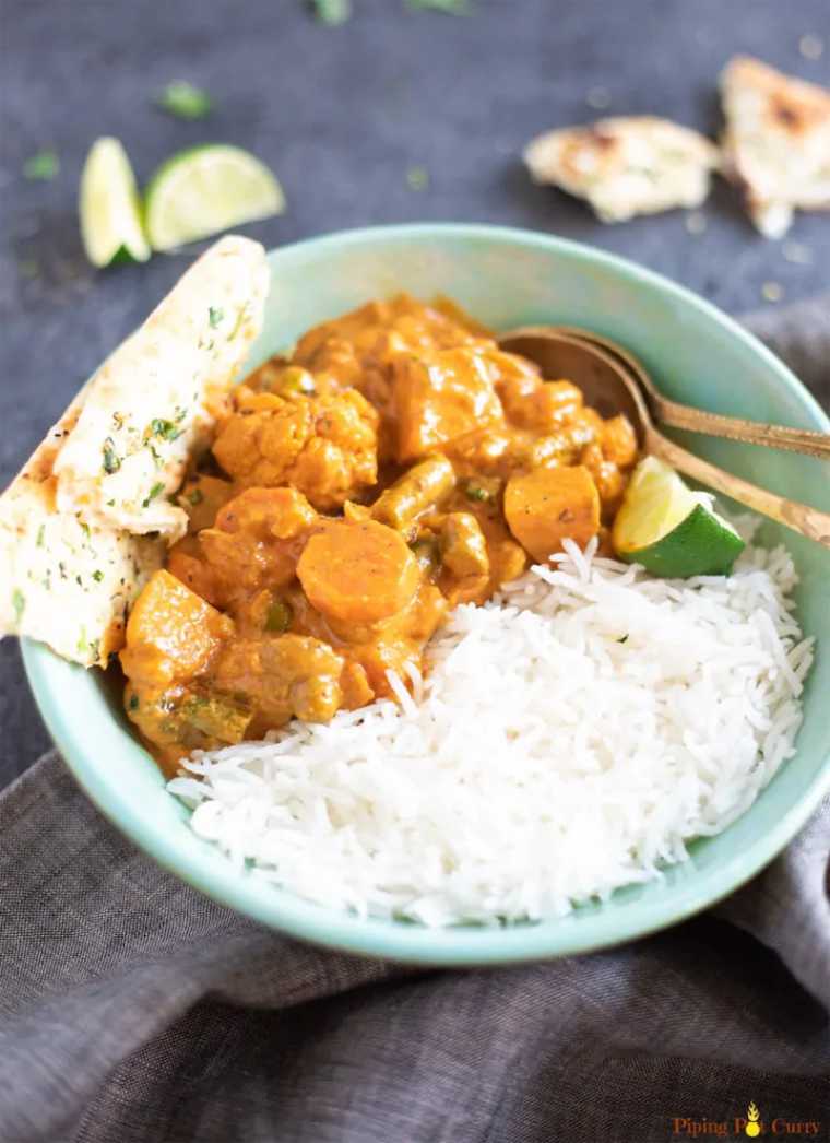 bowl with white rice and vegetable korma next to two spoons on a table