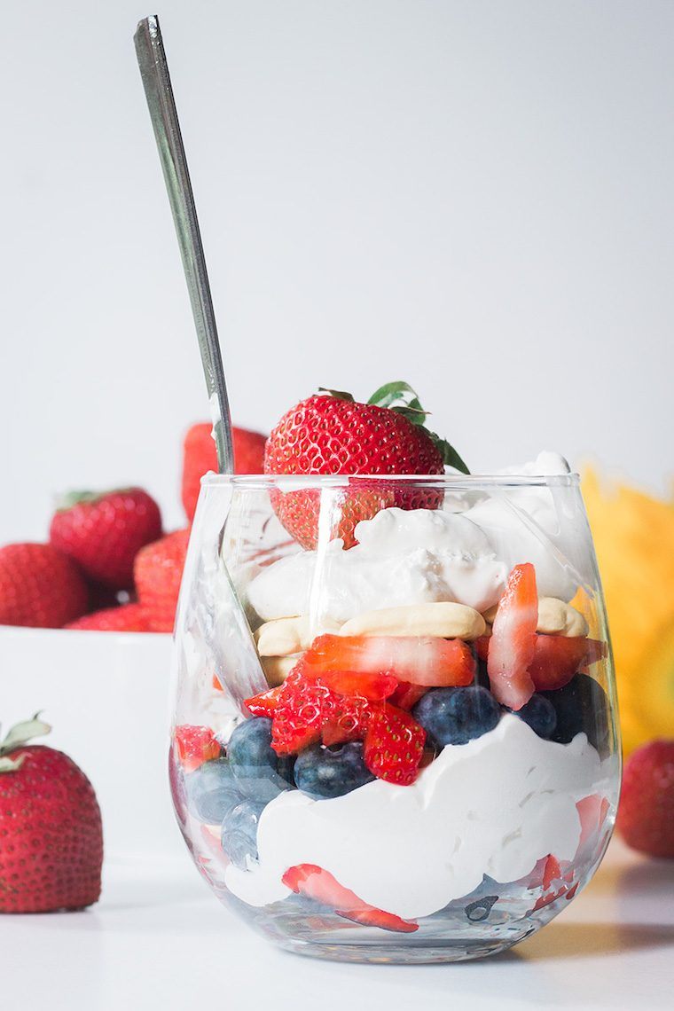 side view of a glass with blueberries, strawberries, coconut whipped cream and a spoon