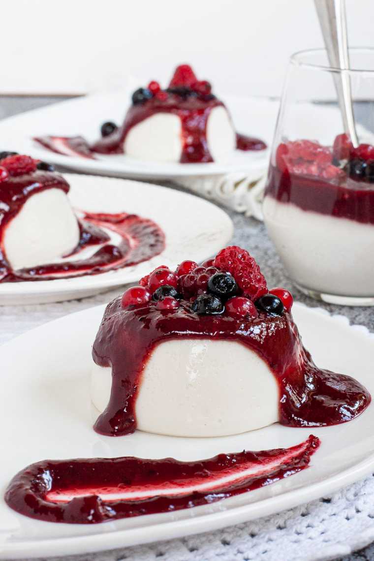 3 white plates with white panna cotta topped with a thick purple sauce and different berries.