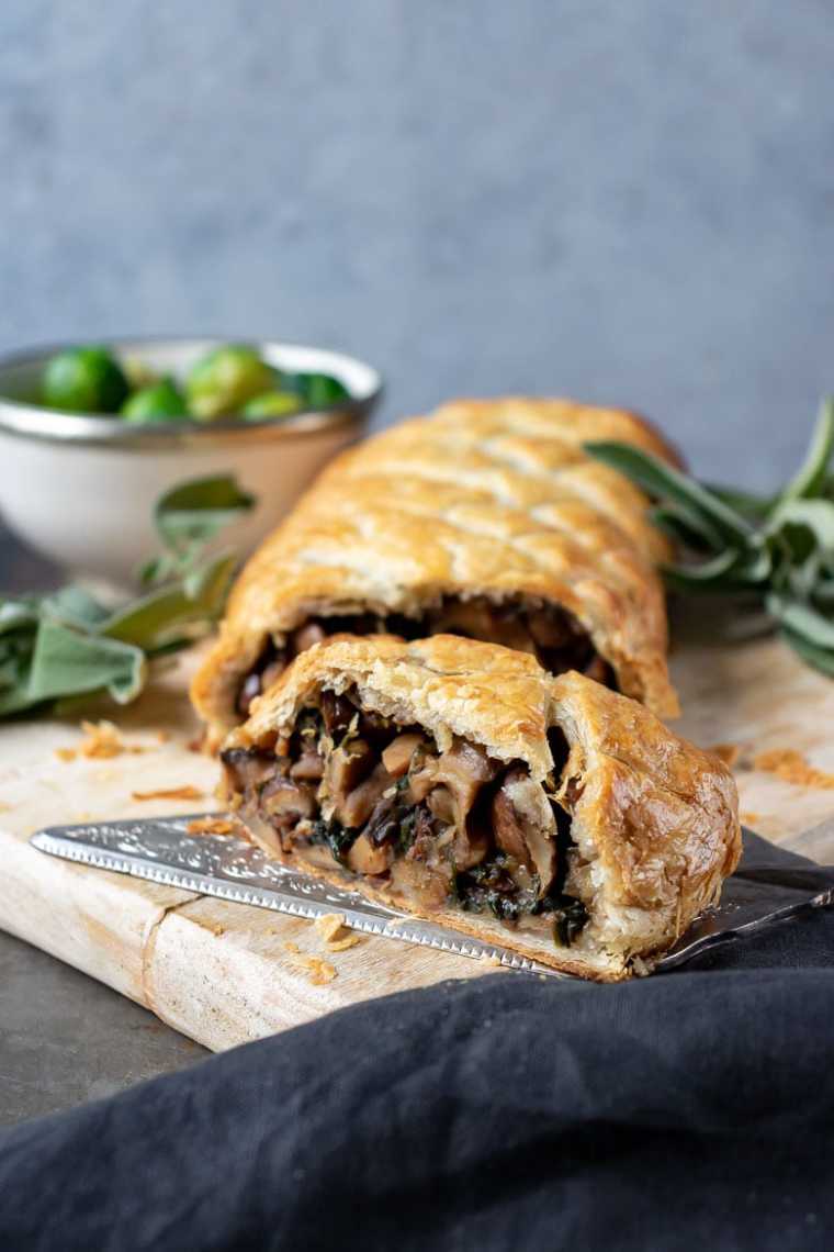 table with a wooden chopping board and a vegan mushroom wellington that's been sliced open