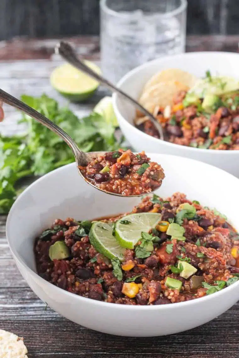 two large white bowls with quinoa veggie chili and slices of lime on a table