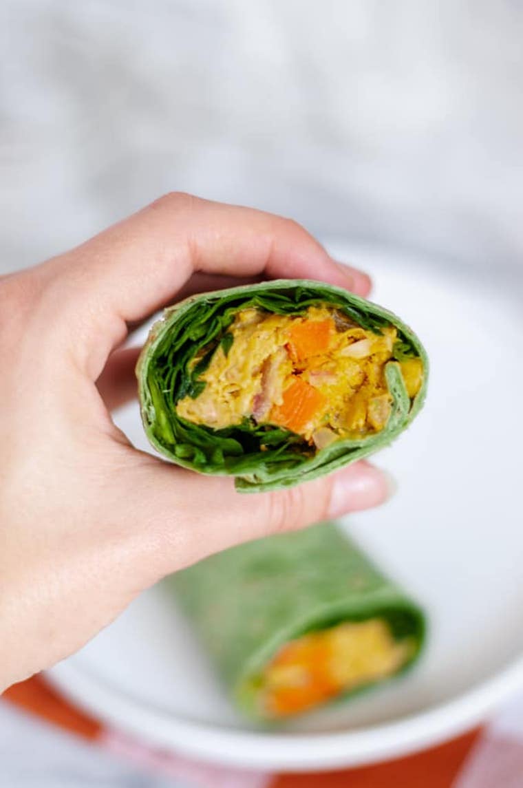 hand holding a green tortilla wrap with lettuce and curried chickpea mash