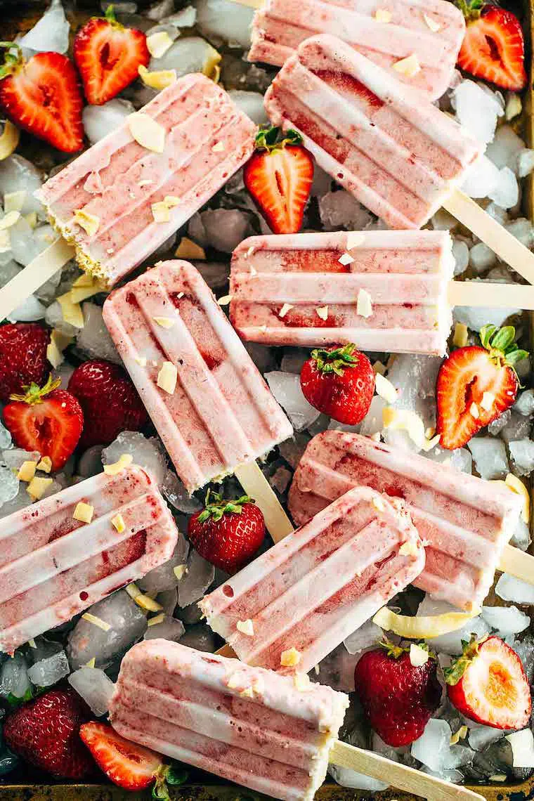 ice cubes on which lie nine homemade strawberry and coconut popsicles which is a great vegan summer dessert