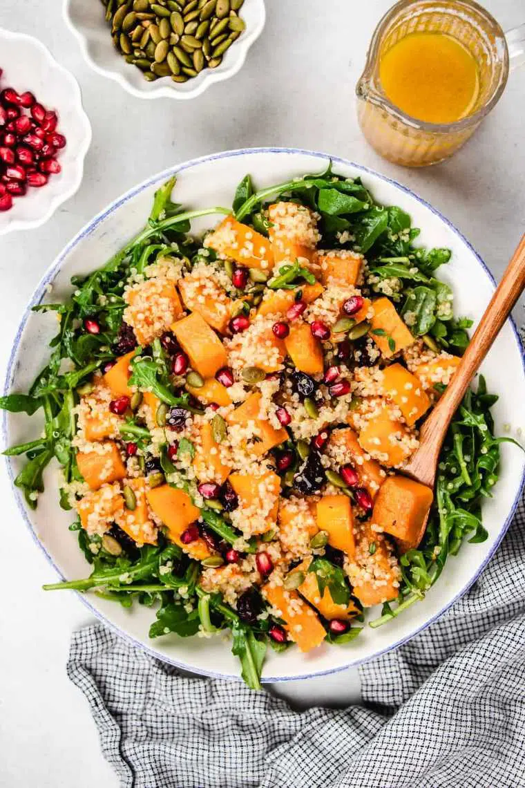 large white bowl on a table with arugula, roasted squash, quinoa and pomegranate seeds