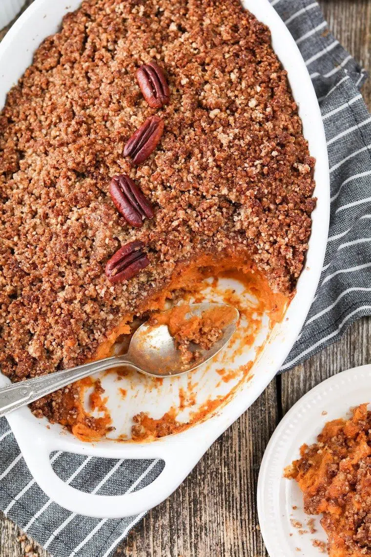 white baking dish with some vegan sweet potato casserole and pecan crumble, some taken out by a spoon