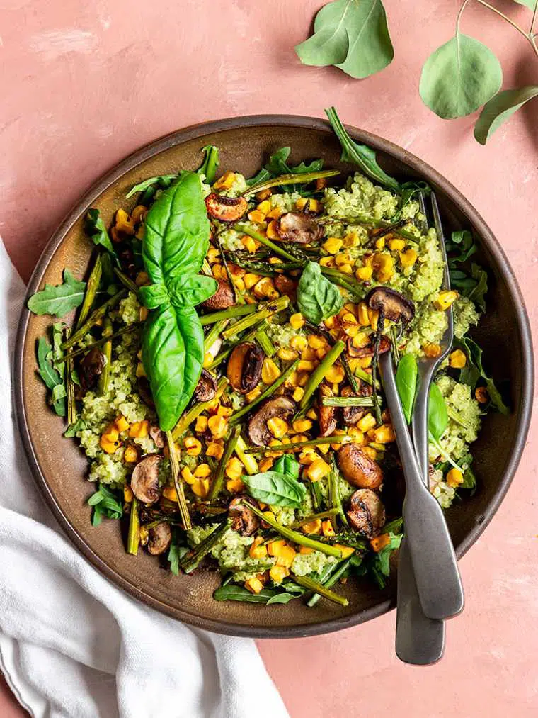 brown bowl on a table with green pesto quinoa, asparagus, corn and arugula