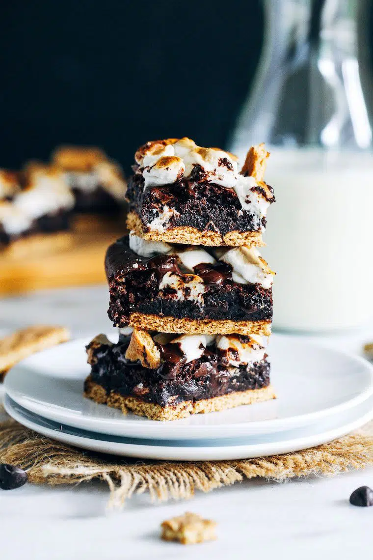 two small white plates where three vegan s'mores brownies are stacked on top of each other