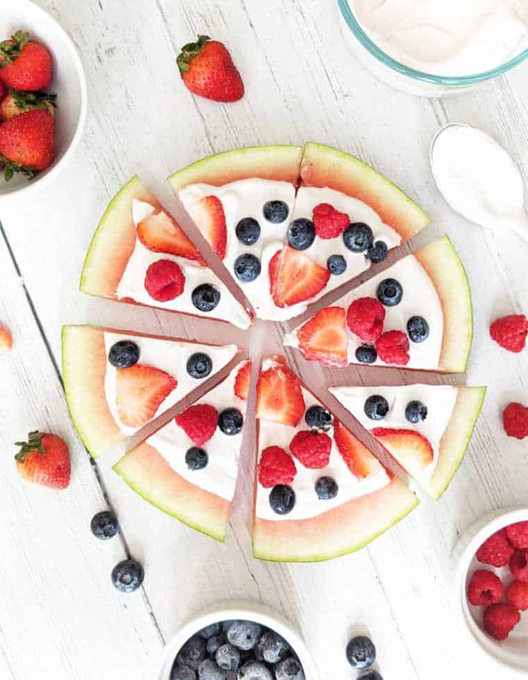 white wooden table with a slice of watermelon that's been cut and decorated with coconut cream and fresh berries
