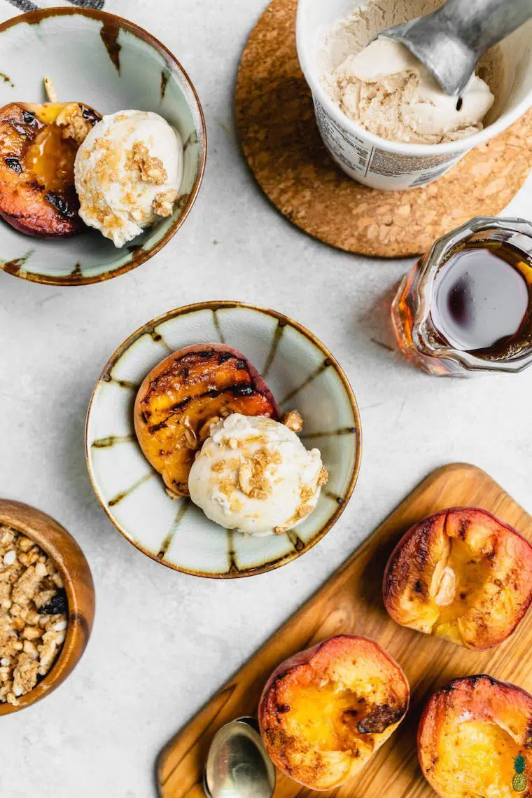 white plate with several bowls of halved grilled peaches with some creamy vegan ice cream