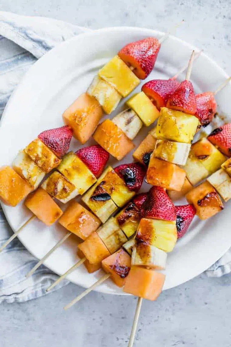 white plate with five grilled strawberry, pineapple, melon and banana kabobs