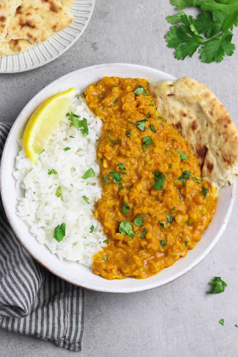 close up of large white bowl with rice, naan, lemon wedge and vegan red lentil dahl