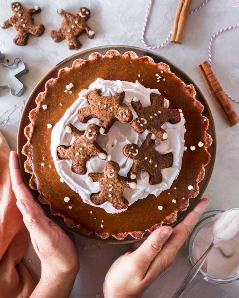 table with winter decor and a homemade gingerbread vegan caramel tart that's been held by two hands