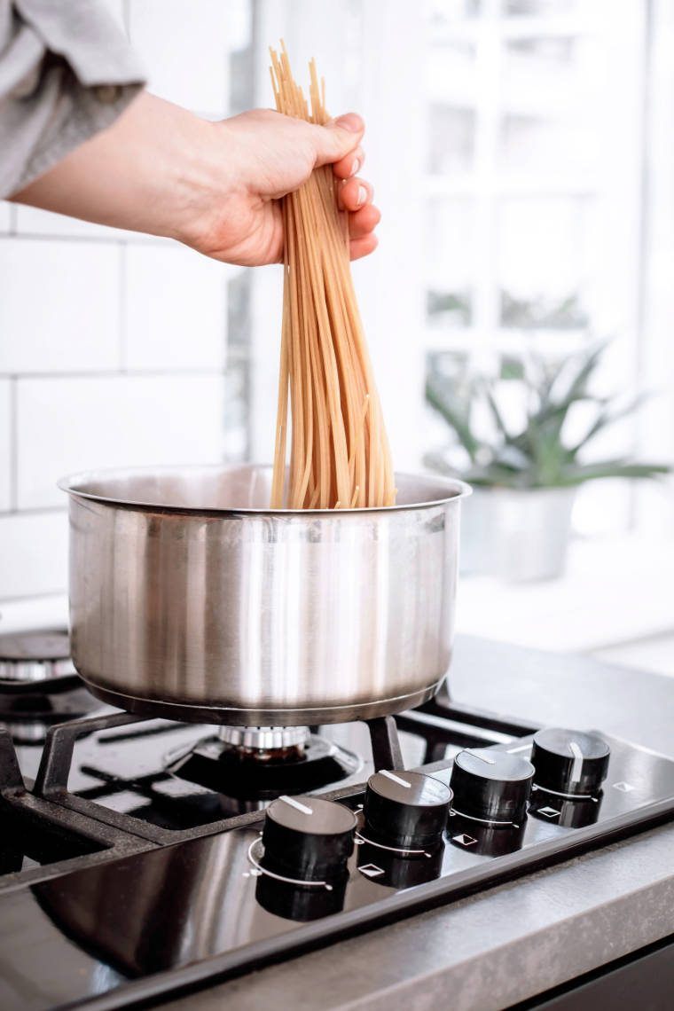 stove with a pot of hot water into which is hand is placing uncooked soba noodles