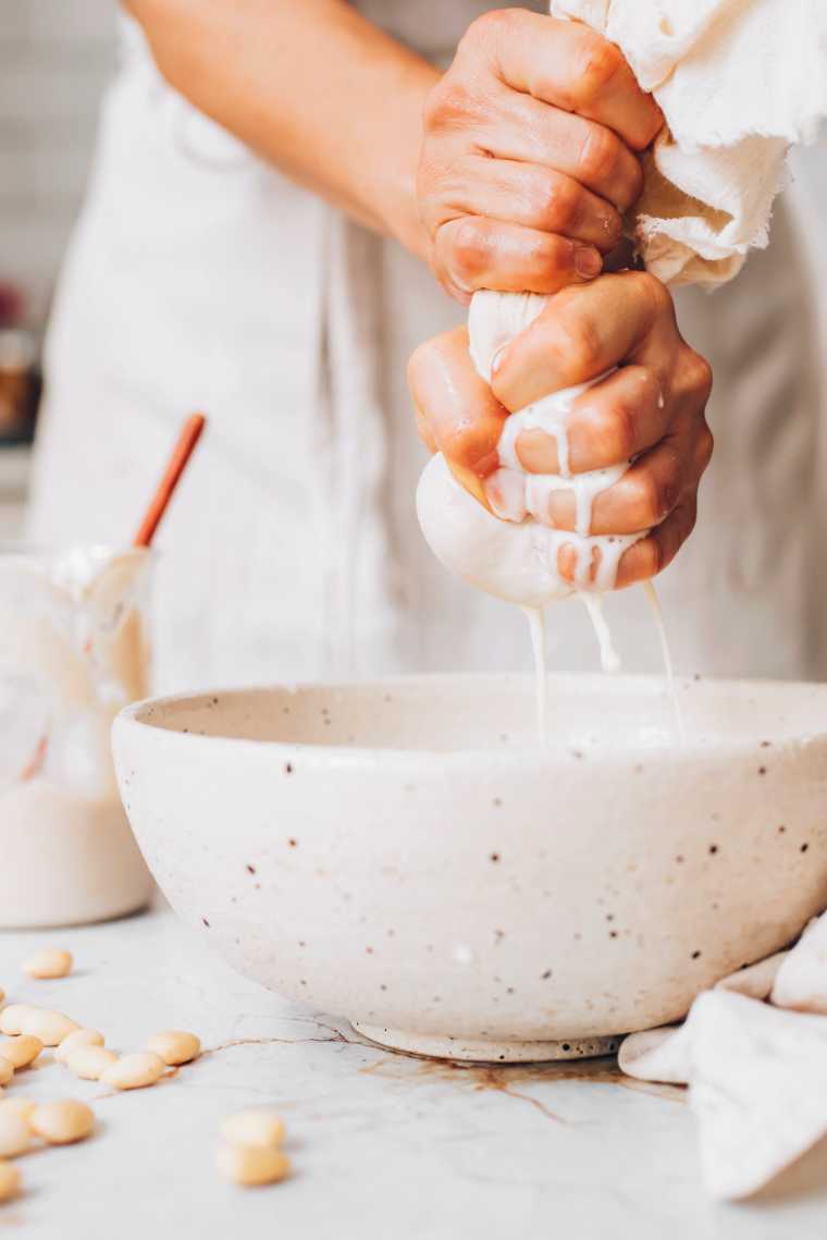 woman squeezing a nut milk bag to make almond milk
