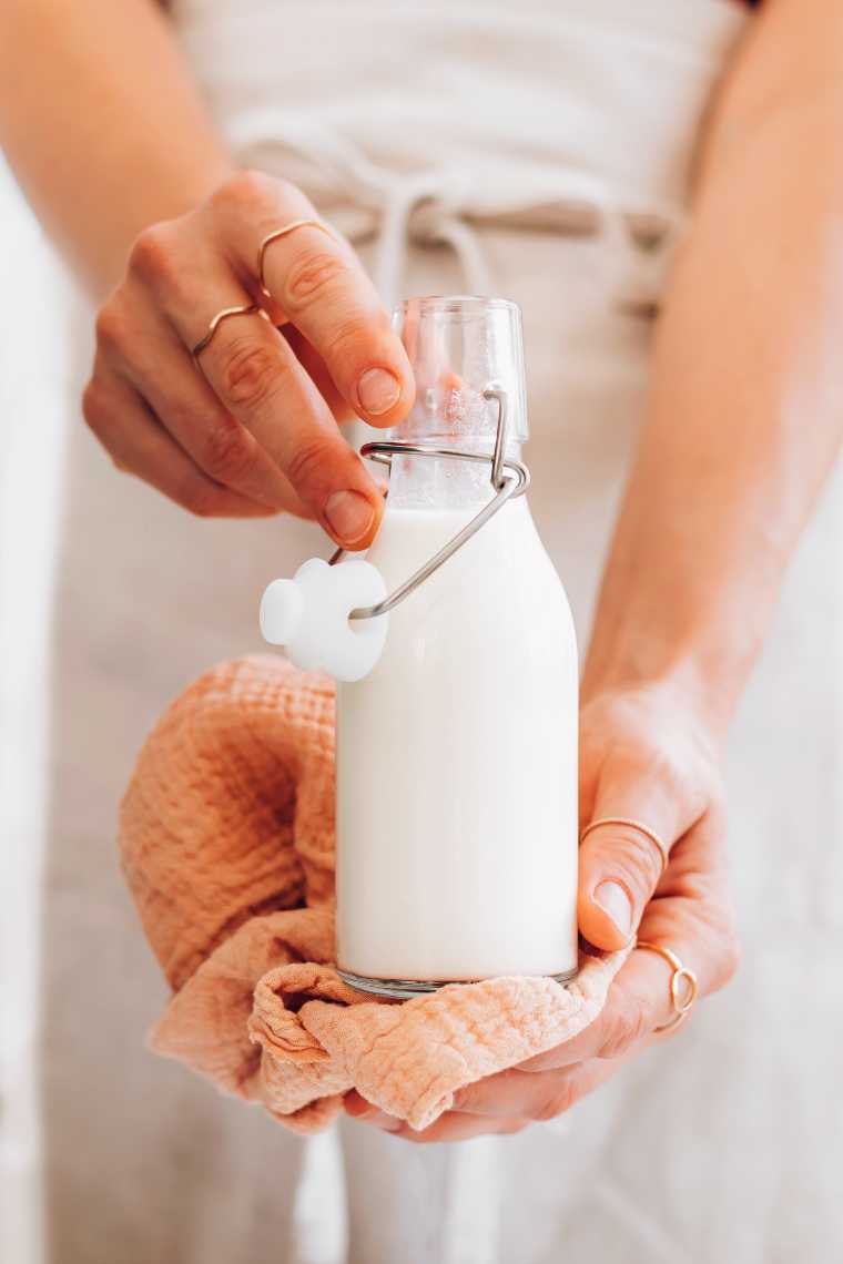 woman in apron holding a glass bottle with homemade almond creamer