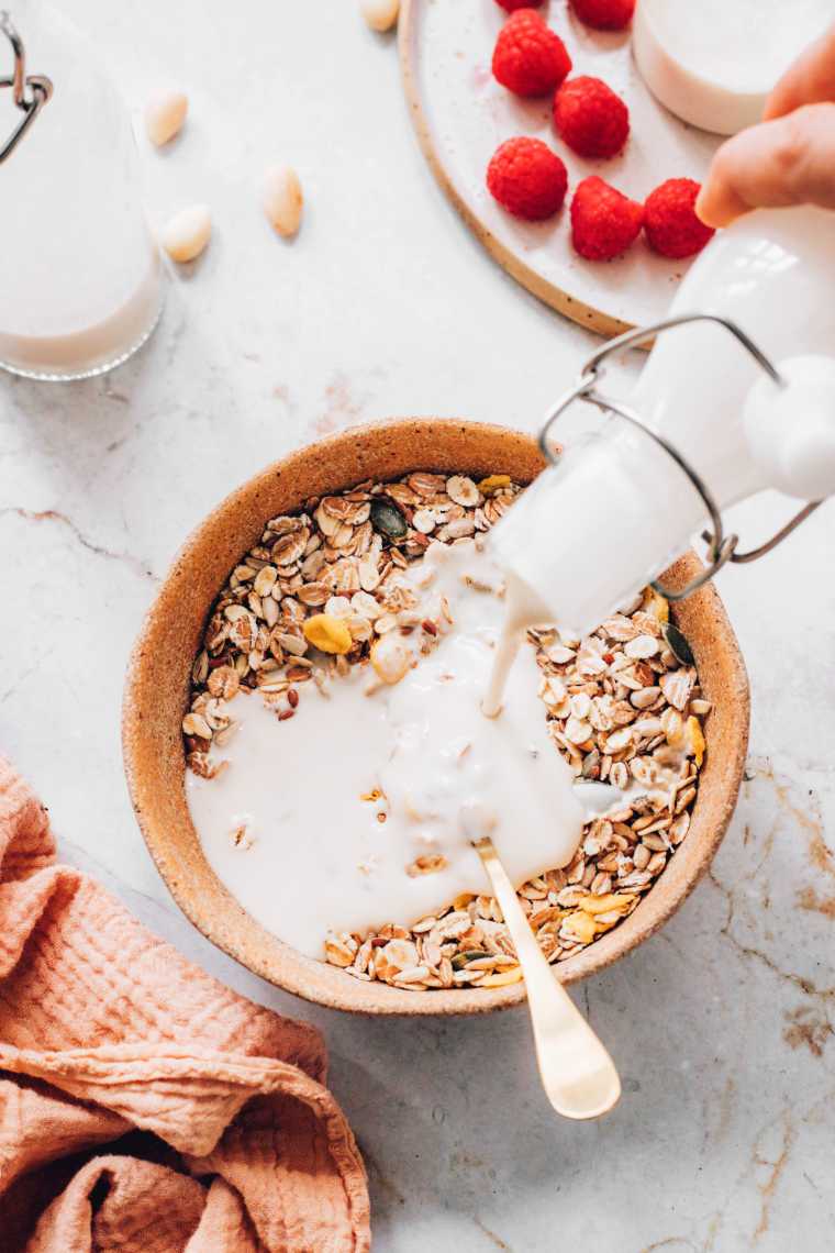 hand pouring dairy free milk over a bowl of oats with a spoon