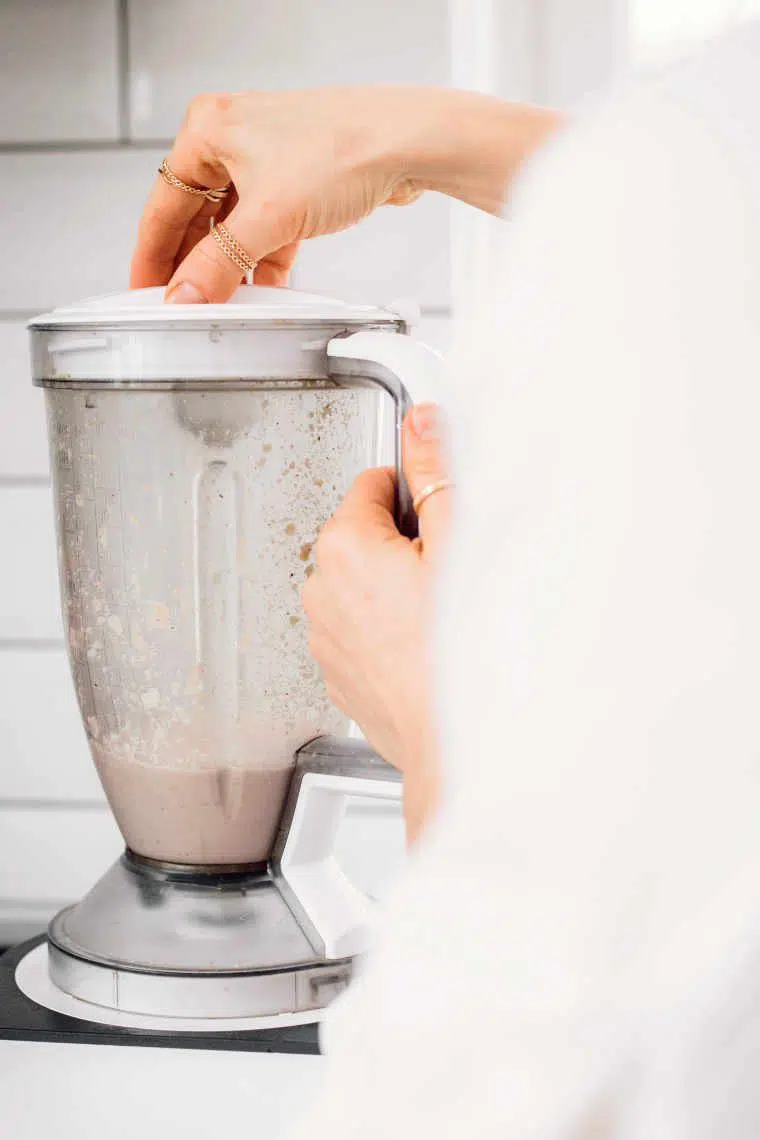 woman standing next to a high speed blender and blending ingredients together to make almond ricotta