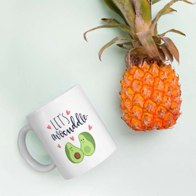 Cute avocado-themed mug on a surface next to a pineapple
