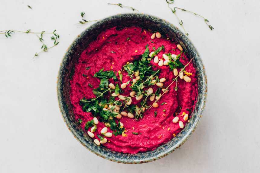 roast beetroot dip in a small bowl with fresh herbs and pine nuts