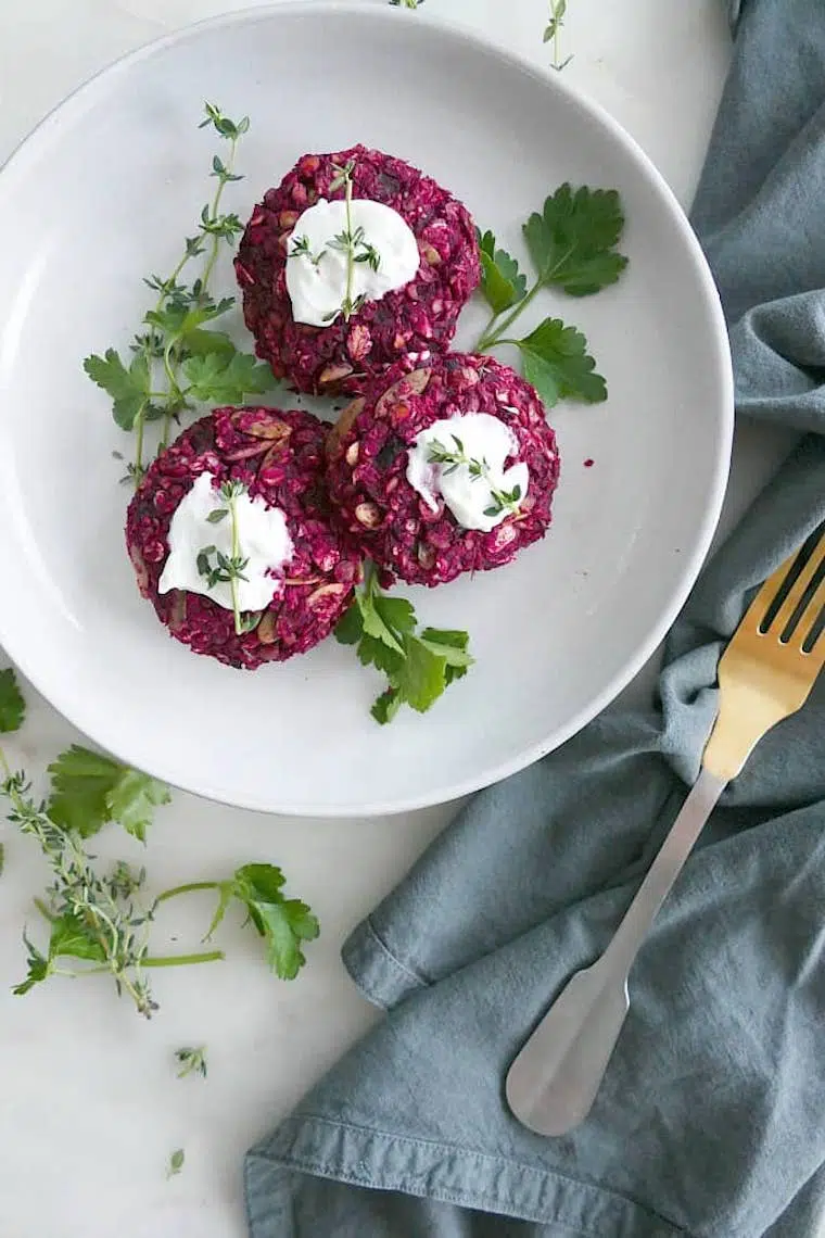 white plate with three pink beet lentil caked and fresh herbs on a table