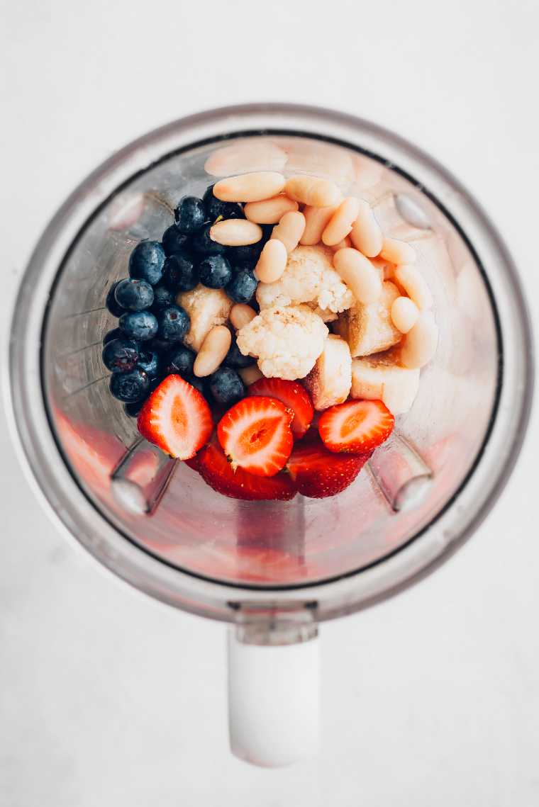 fresh strawberries, blueberries, white beans, banana and cauliflower in blender jar