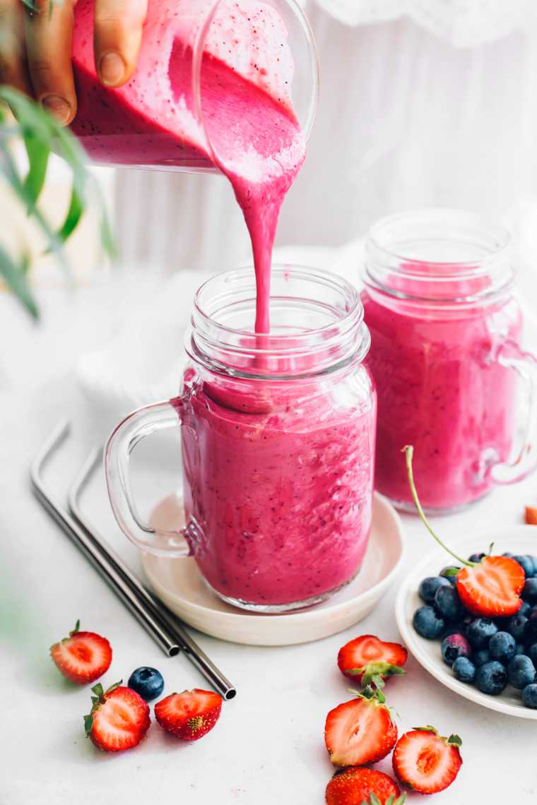 woman in white dress pouring homemade berry bean smoothie in glass jars