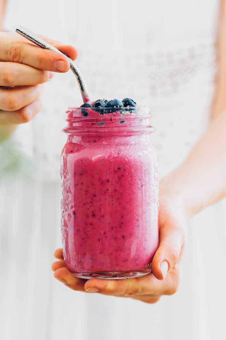 woman in white dress holding a glass jar with homemade strawberry and blueberry smoothie in her hands