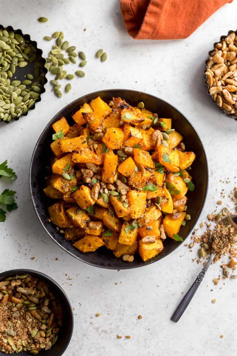 black bowl with cubed roasted butternut squash, nuts and seeds