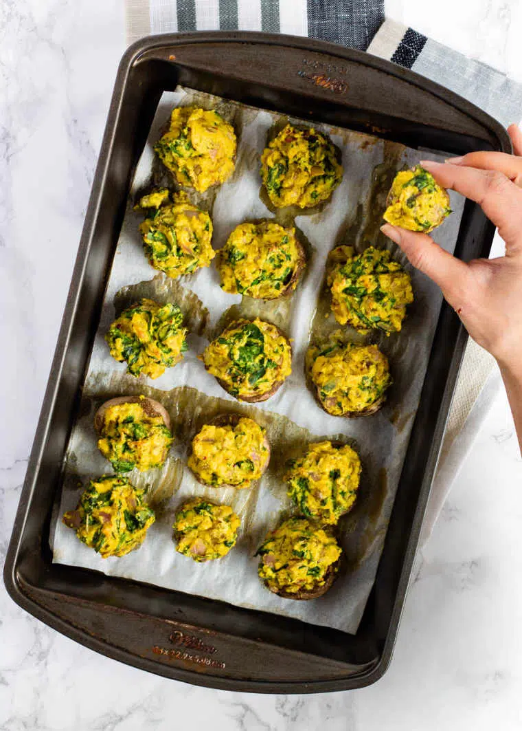 baking dish with yellow stuffed mushrooms one of which is taken by a hand