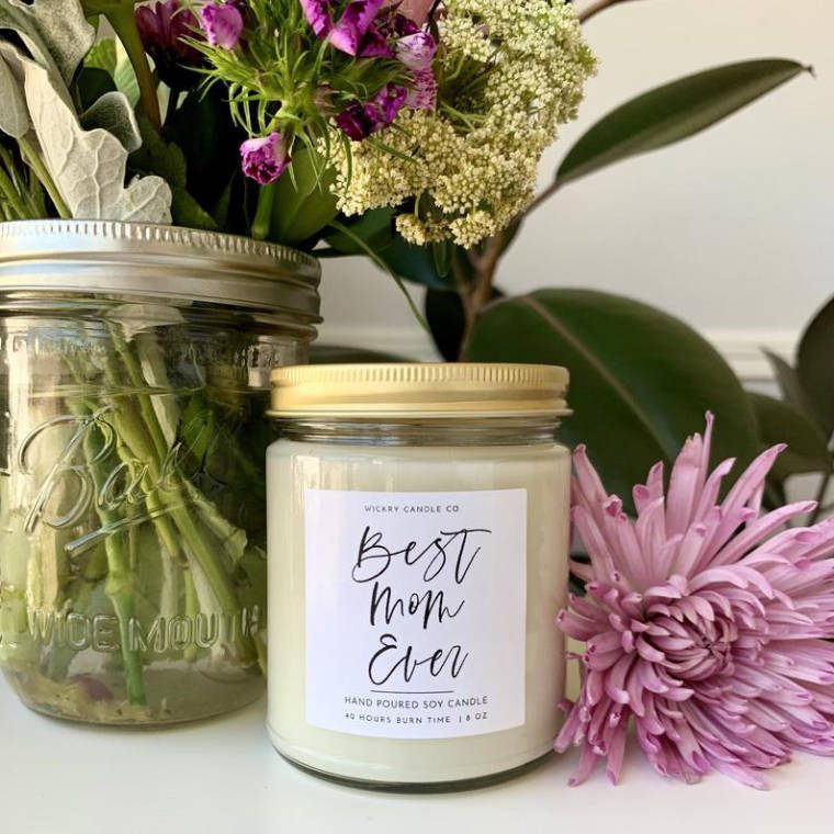 flowers on a table with a soy candle in a glass jar with text on it saying "best mom ever"