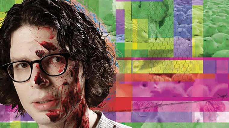 Man with glasses having blood splatters on his face in front of a background of colorful geometric shapes