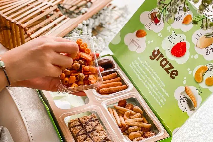 Graze snack box with a woman's hand reaching for a savory vegan snack