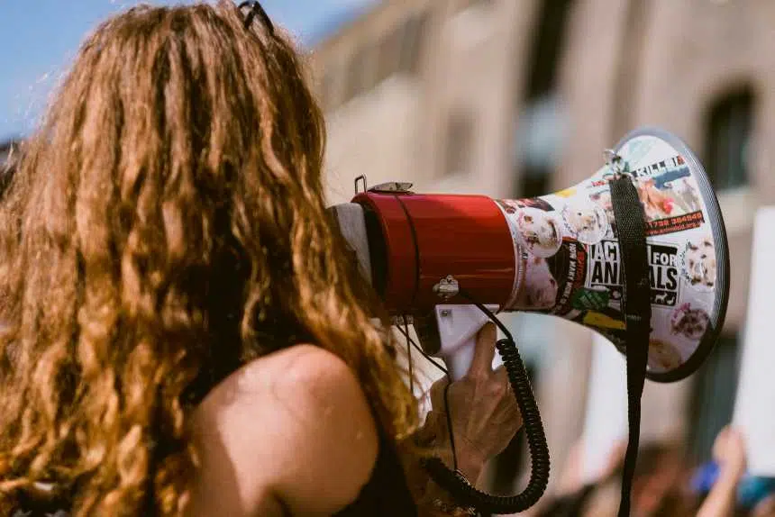 Closeup of curly-haired woman speaking into megaphone with lots of vegan stickers