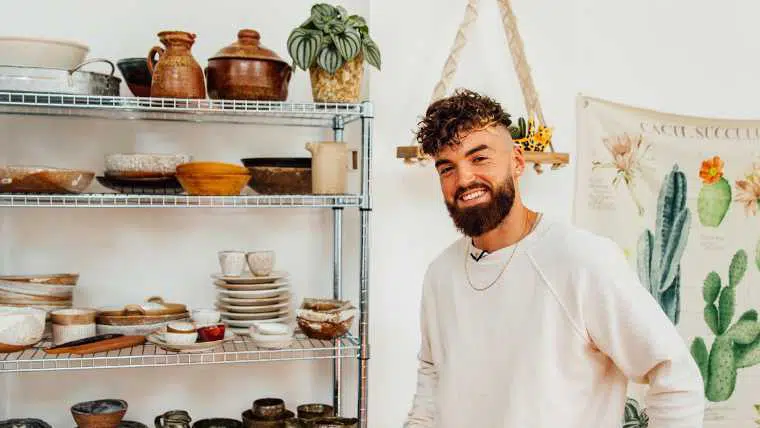 Gaz from Avantgarde Vegan smiling and standing next to shelf with lots of kitchenware