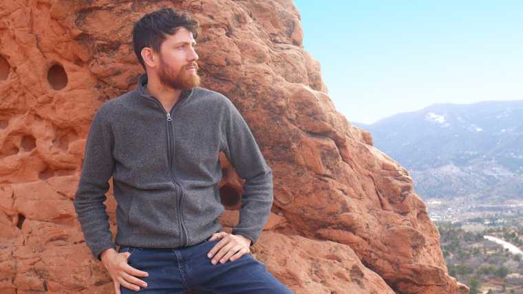Mic from Mic The Vegan standing in front of red rocks looking sideways, hands resting on his hip,
